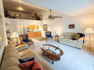 Living area with vaulted ceiling, light colored carpet, ceiling fan, and a chandelier