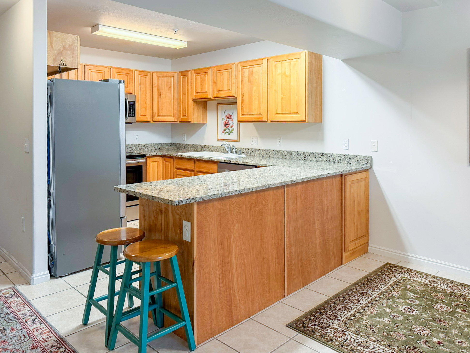 Kitchen with stainless steel appliances, a peninsula, light tile patterned floors, light stone counters, and a breakfast bar area