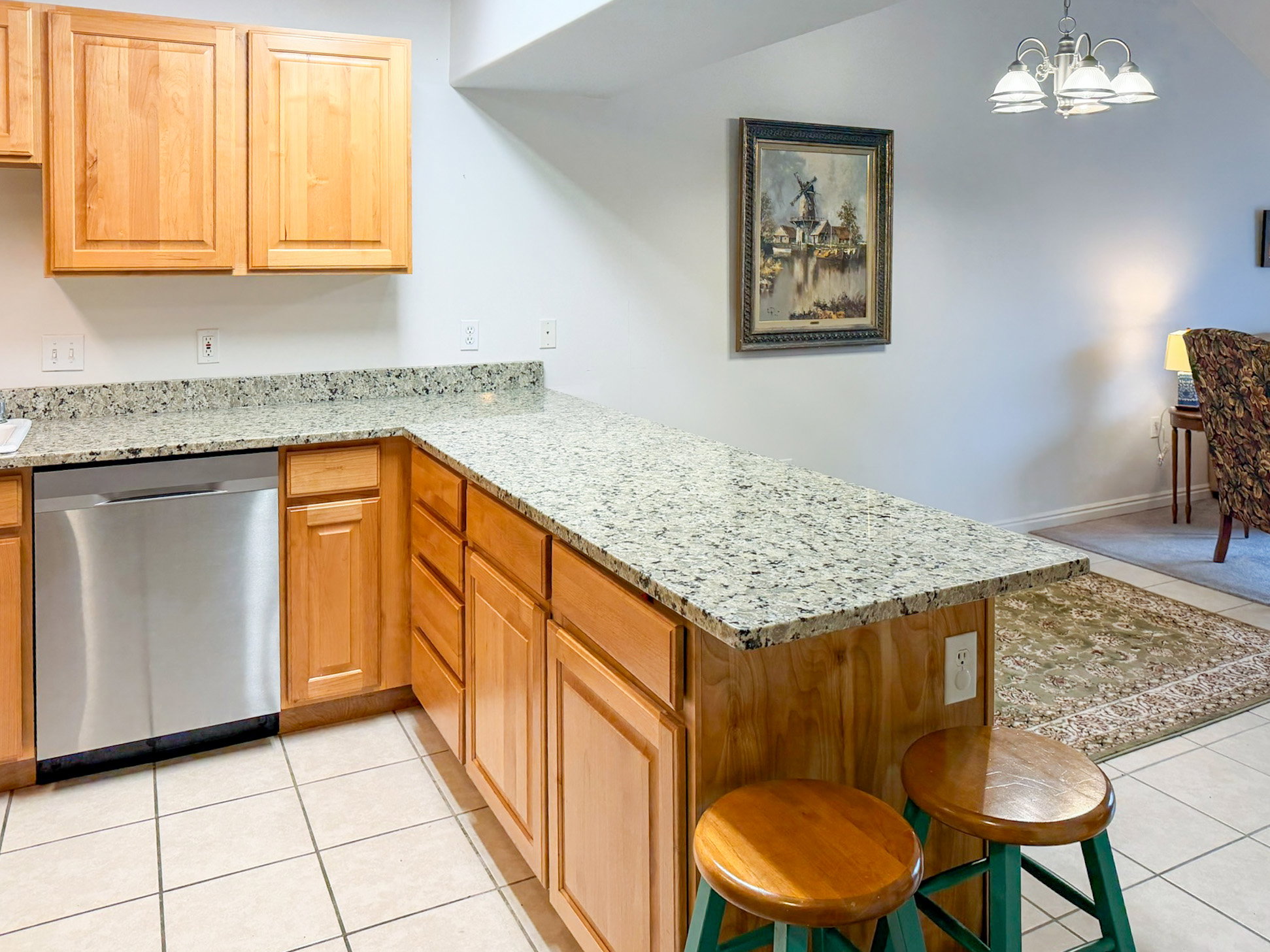 Kitchen with light stone countertops, stainless steel dishwasher, a peninsula, light tile patterned floors, and a chandelier