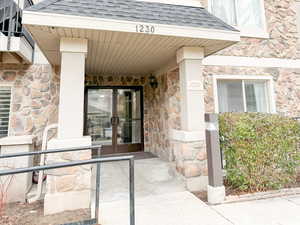 Doorway to property with stone siding, a shingled roof, and covered porch