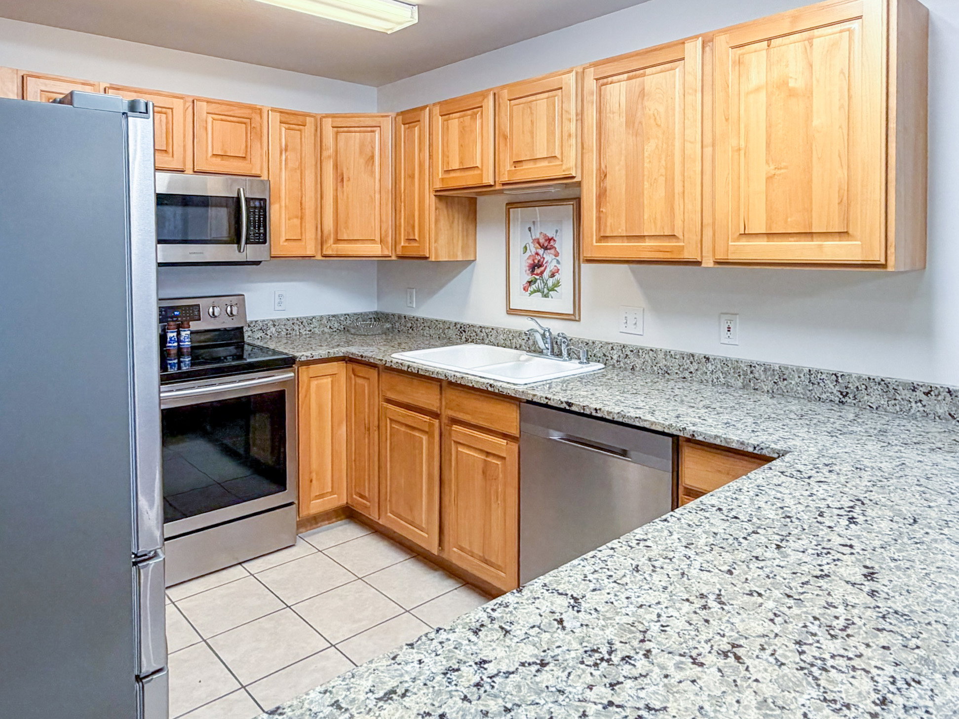 Kitchen with stainless steel appliances, light stone counters, light tile patterned flooring, and light wood finish cabinetry
