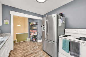 Kitchen with white electric stove, light wood-style flooring, white cabinets, light stone countertops, and pendant lighting