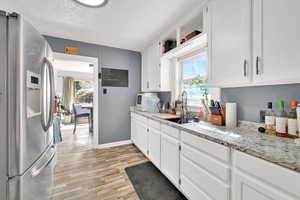 Kitchen with stainless steel fridge, white cabinetry, light wood-style flooring, light stone countertops, and a textured ceiling