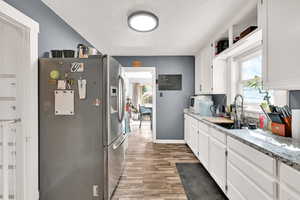 Kitchen featuring stainless steel fridge, white cabinetry, a textured ceiling, light wood-style flooring, and light stone countertops