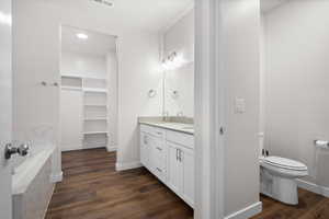 Full bathroom with dark wood-type flooring, double vanity, a walk in closet, and a garden tub