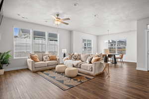 Living room with dark wood-style flooring, a ceiling fan, plenty of natural light, and a textured ceiling