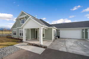 View of front of home with concrete driveway, board and batten siding, an attached garage, roof with shingles, and covered porch