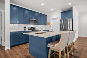Kitchen with blue cabinetry, stainless steel appliances, a center island with sink, a kitchen breakfast bar, and dark wood-type flooring