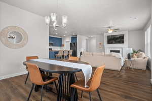 Dining room featuring a fireplace, dark wood-style floors, hanging lights, and ceiling fan