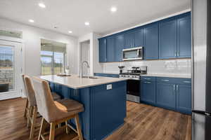 Kitchen with blue cabinets, stainless steel appliances, an island with sink, and recessed lighting