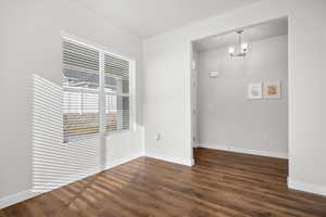 Unfurnished room with dark wood-style floors and a chandelier