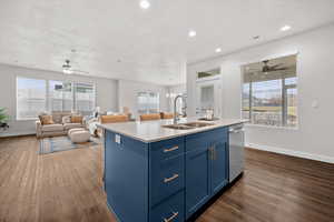 Kitchen featuring blue cabinets, a ceiling fan, suspended lighting, open floor plan, and an island with sink