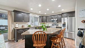 Kitchen featuring stainless steel appliances, light stone countertops, light wood finished floors, a kitchen breakfast bar, and a center island