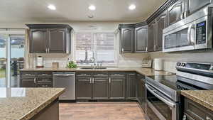 Kitchen with stainless steel appliances, recessed lighting, light wood-style flooring, light stone countertops, and a textured ceiling
