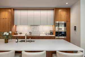 Kitchen featuring modern cabinets, two tone cabinetry, a breakfast bar area, double oven, and light stone countertops