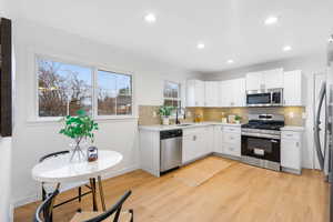 Kitchen featuring stainless steel appliances, white cabinetry, light wood-style floors, light stone countertops, and recessed lighting