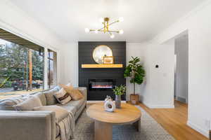 Living room featuring light wood-style floors, a fireplace, suspended lighting, and crown molding