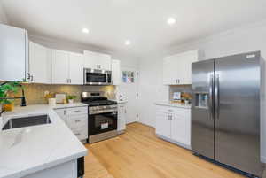 Kitchen featuring stainless steel appliances, light wood finished floors, white cabinets, ornamental molding, and recessed lighting