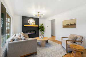 Living area with light wood-style flooring, crown molding, a fireplace, and a chandelier
