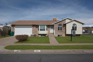 Ranch-style house featuring brick siding, a garage, driveway, a front lawn, and a chimney