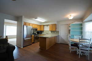 Kitchen with stainless steel appliances, light counter tops, a peninsula, dark flooring, and wood finish cabinets