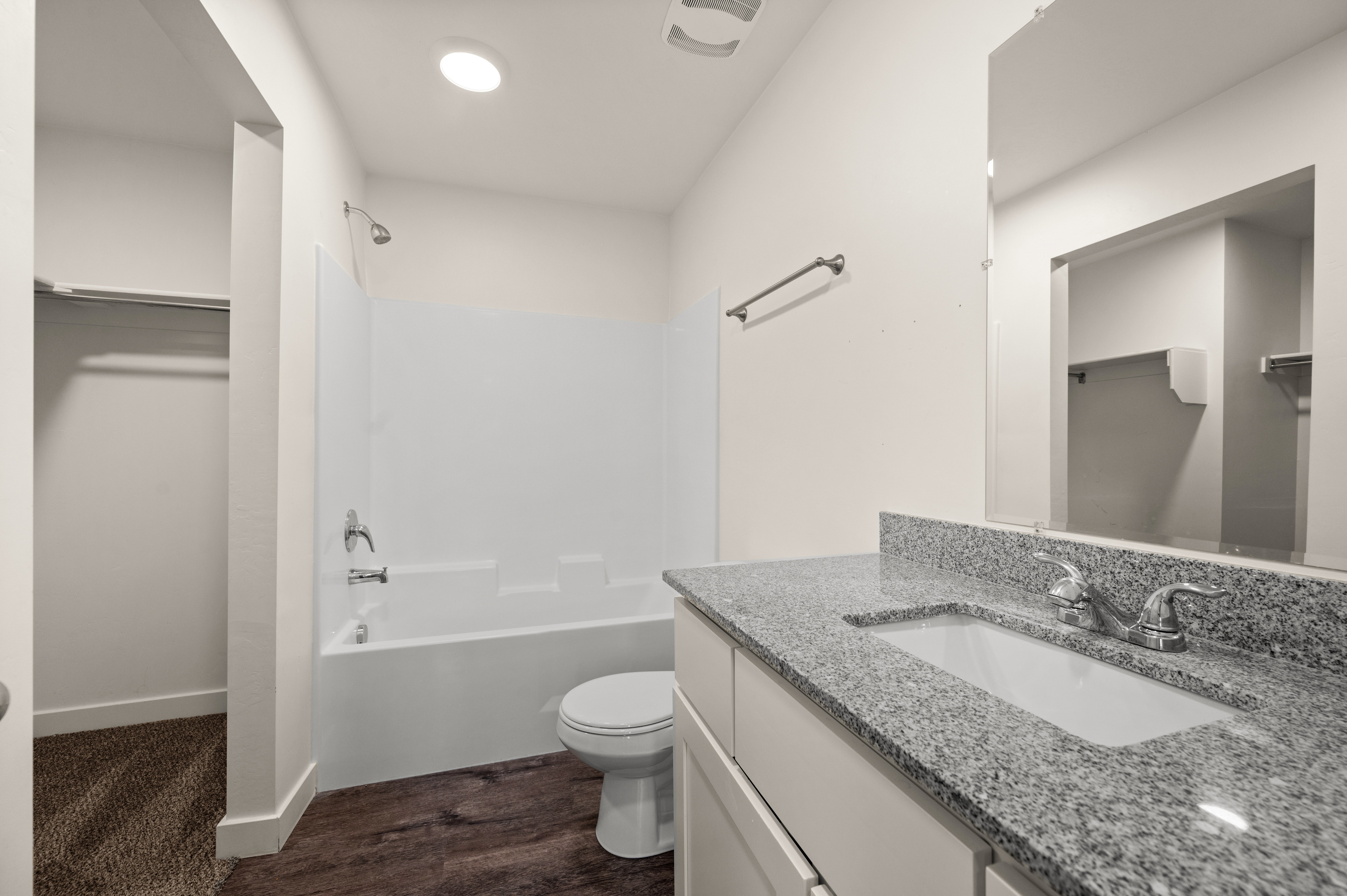Bathroom featuring a granite countertop vanity with an integrated sink, a full-width mirror, a tub-shower combination with white surround, and wood-finish flooring