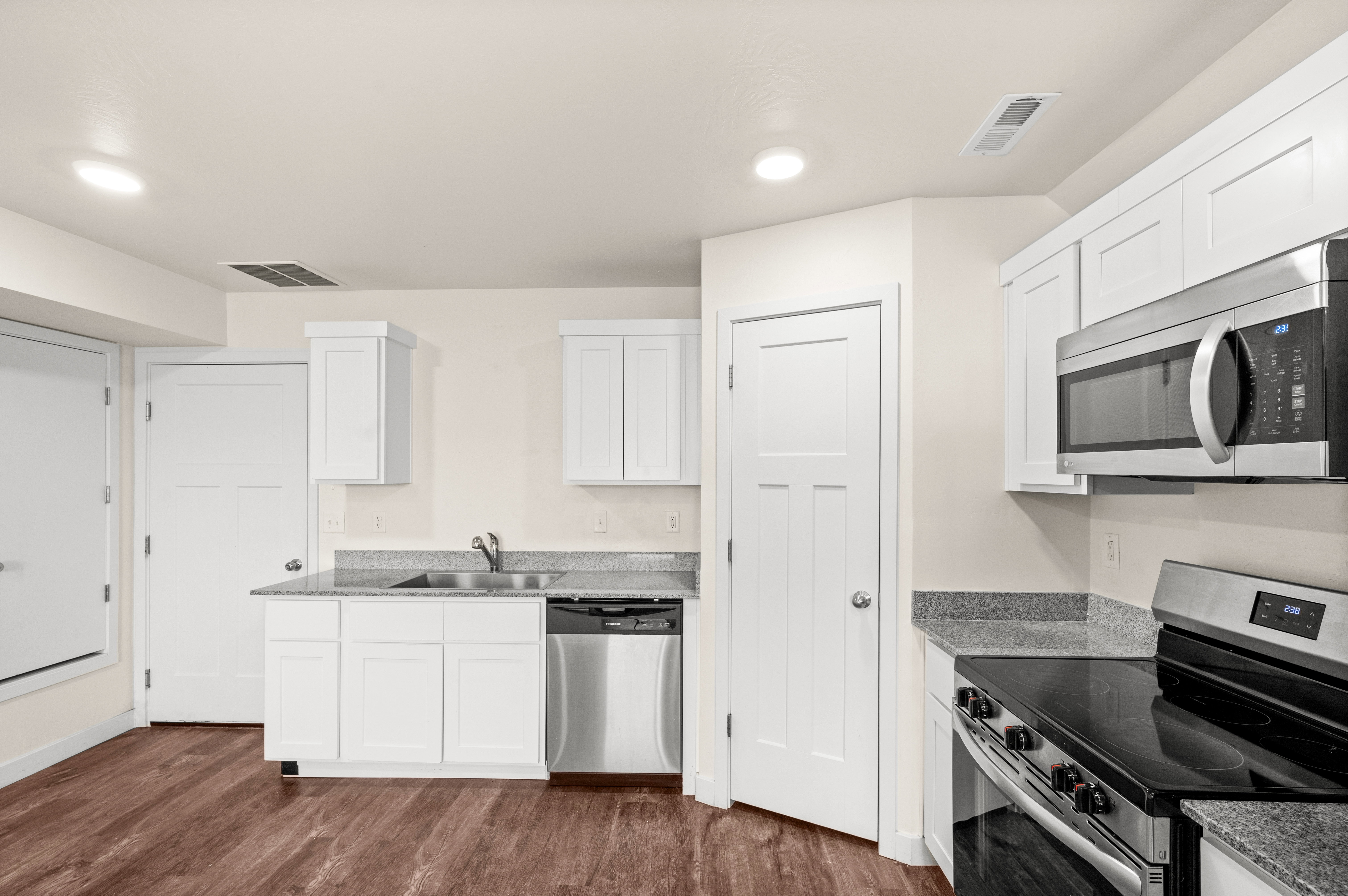 Kitchen featuring wood-finish flooring, white cabinetry, speckled countertops, stainless steel appliances, and recessed lighting