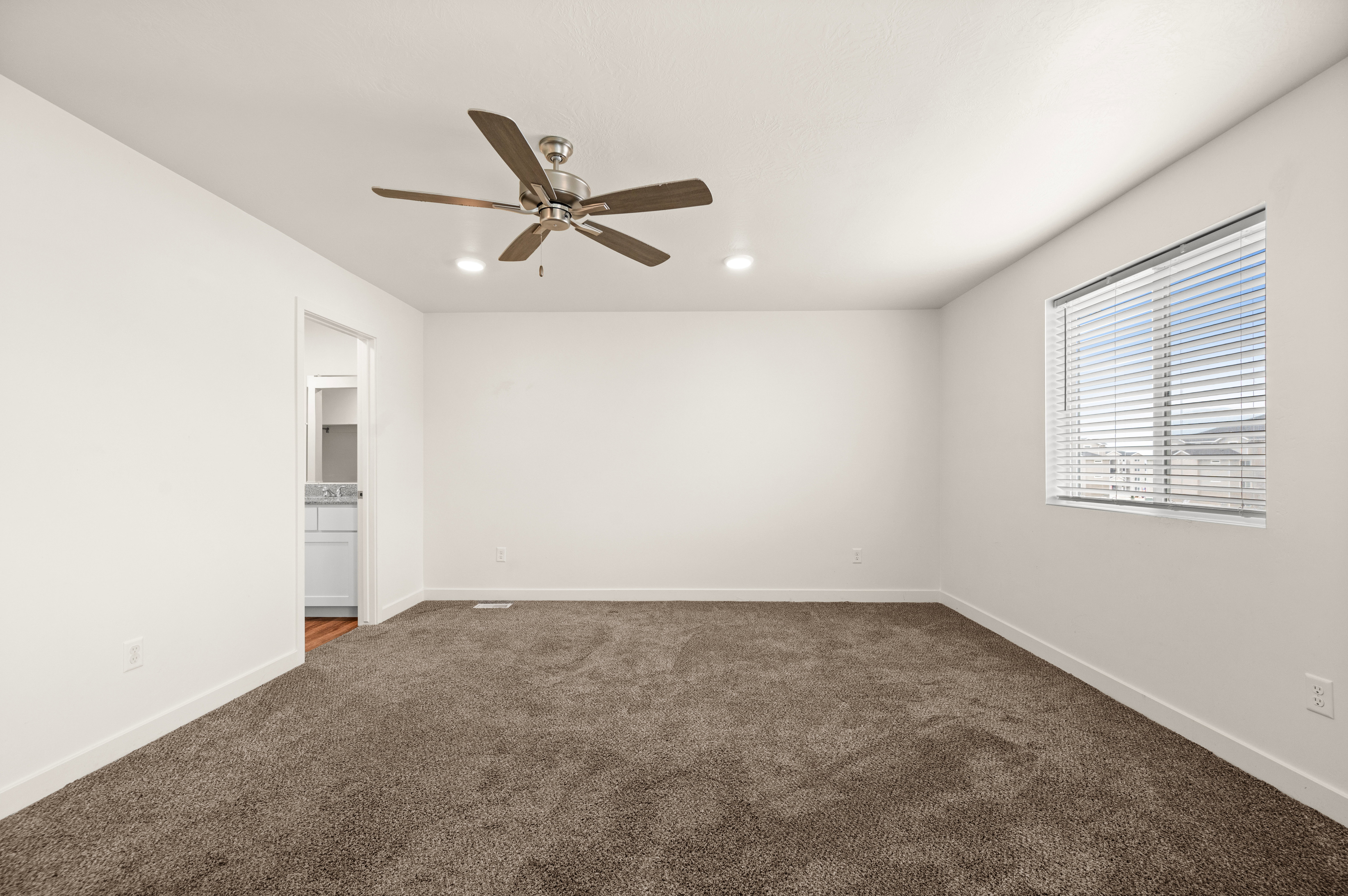 Spacious room featuring neutral carpeting, a ceiling fan, recessed lighting, and a large window with horizontal blinds