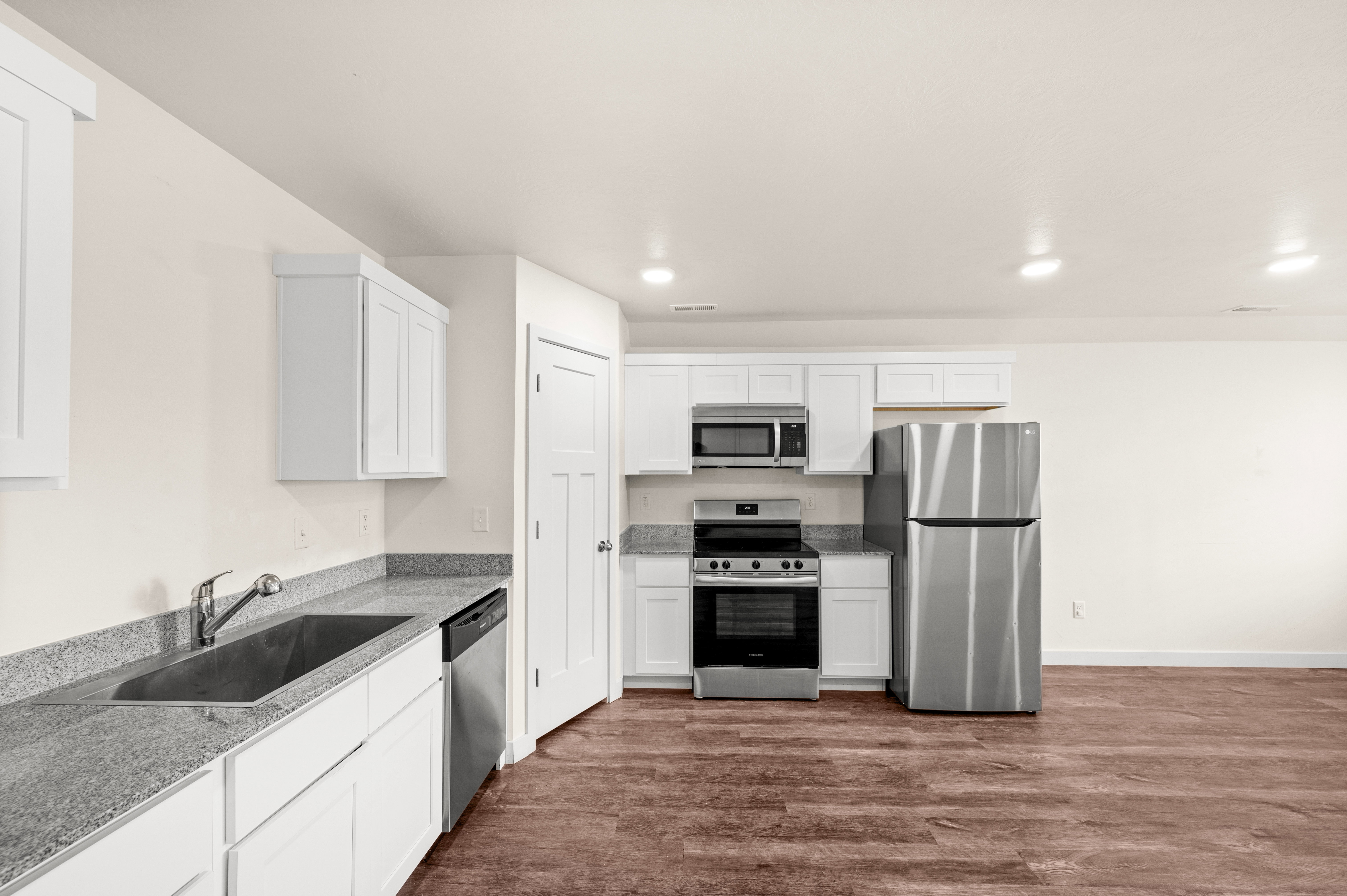 Kitchen featuring white cabinetry, grey stone countertops, stainless steel appliances, a stainless steel sink, and wood-finish flooring