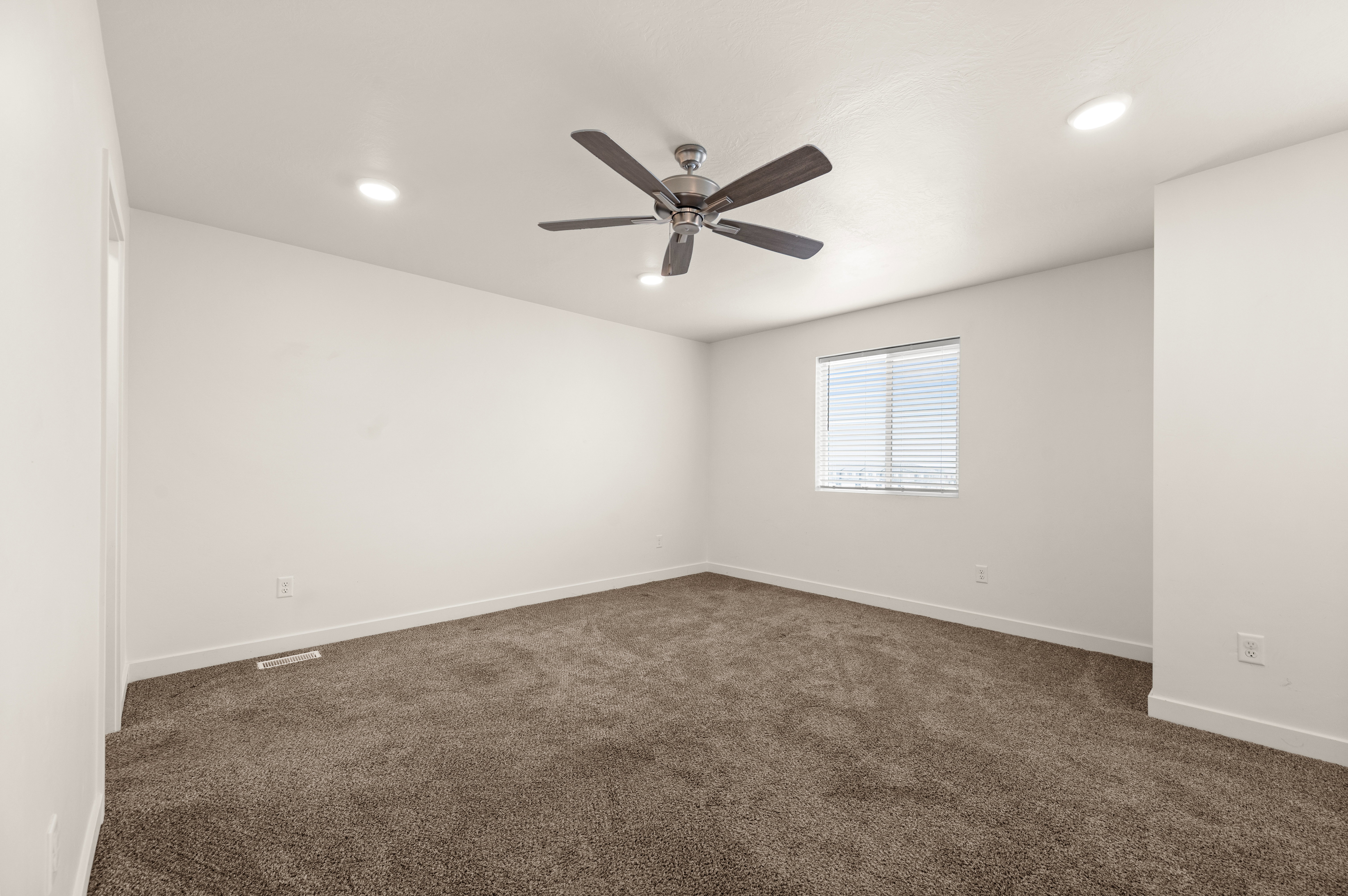 Spacious room featuring neutral carpeting, white walls, a single window with blinds, recessed lighting, and a ceiling fan
