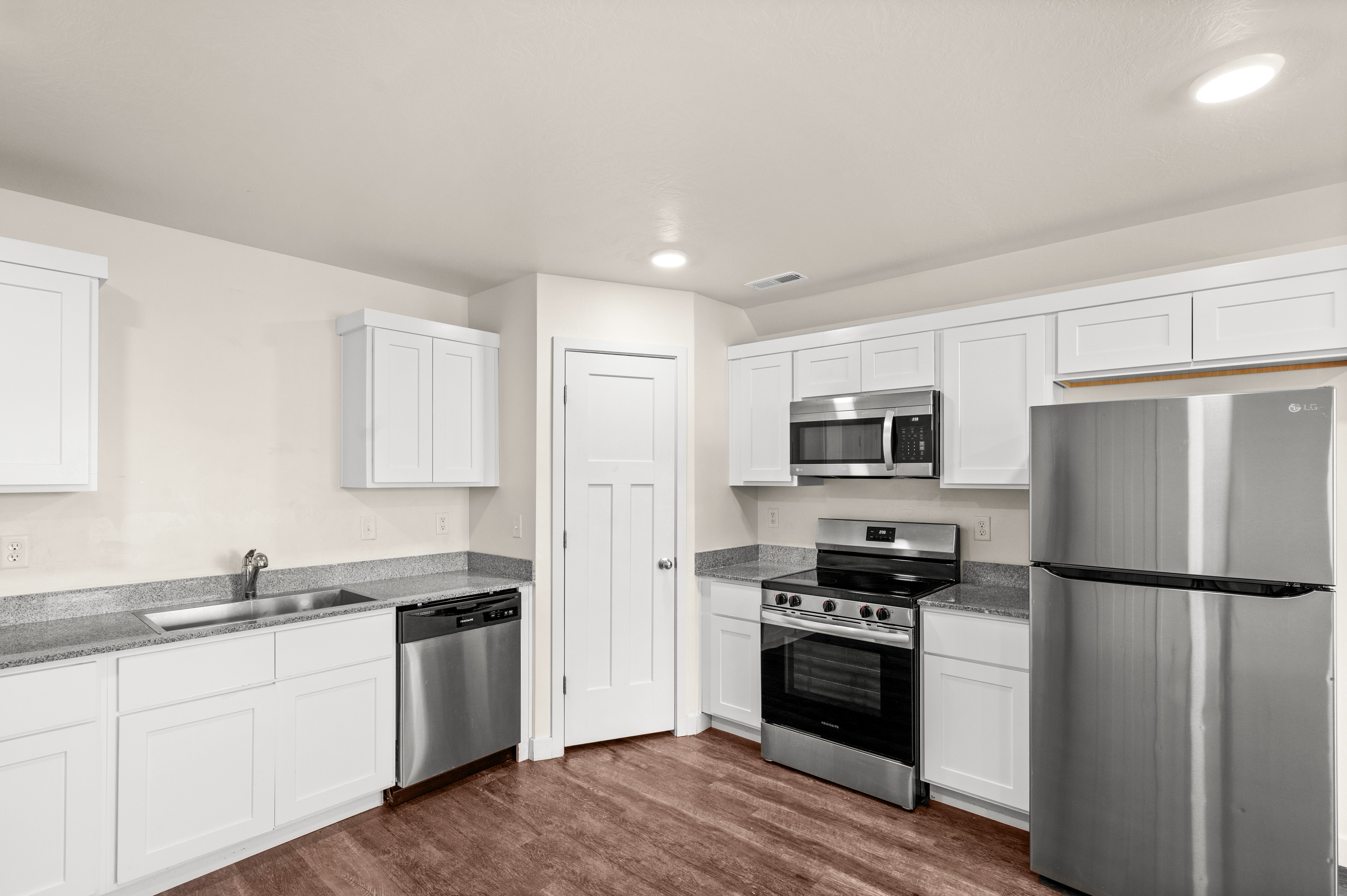 Kitchen featuring white shaker cabinetry, stainless steel appliances, speckled countertops, wood-finish flooring, and recessed lighting