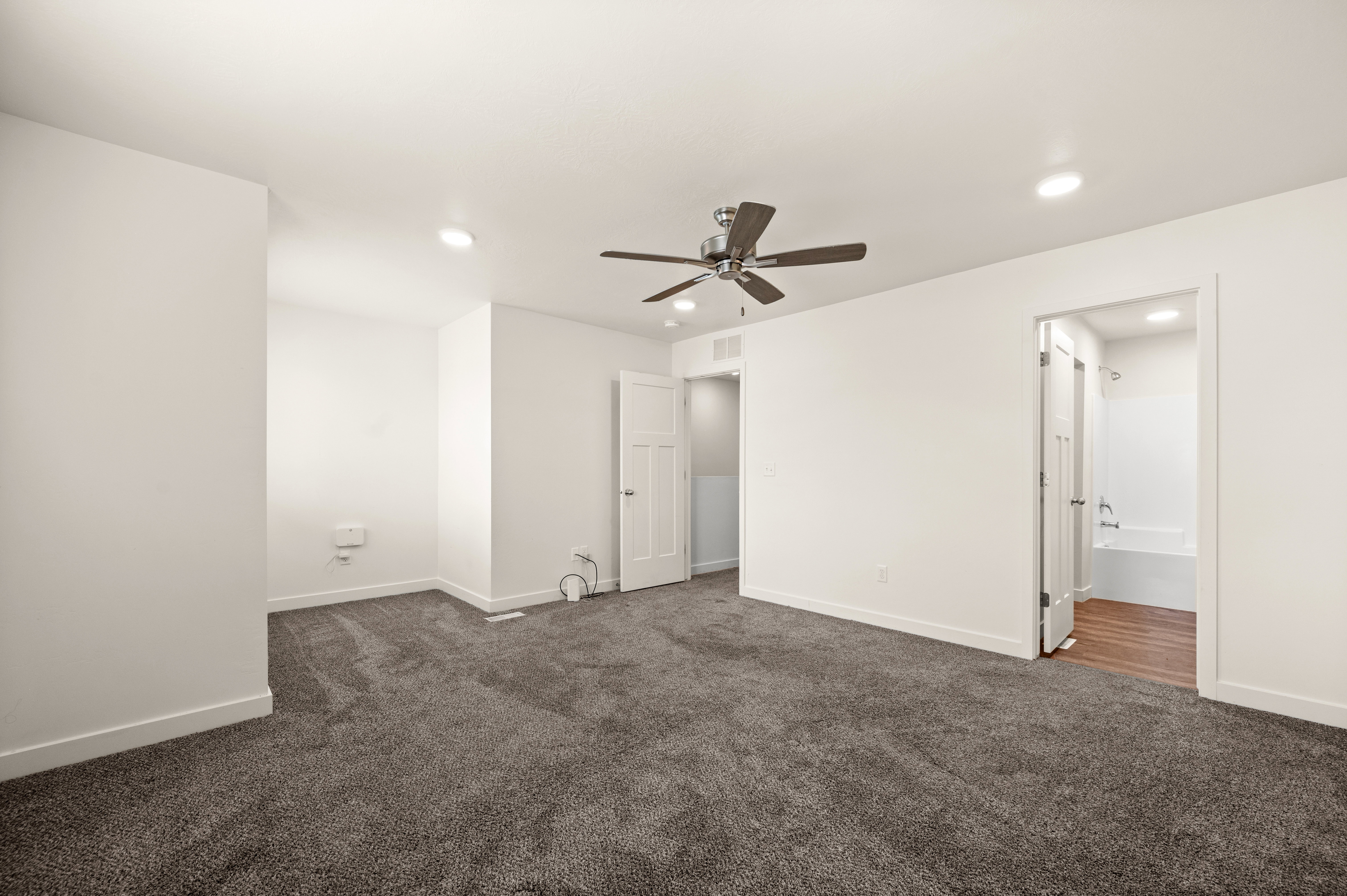 Spacious room featuring neutral carpeting, a ceiling fan, recessed lighting, and a doorway to a bathroom with wood-finish flooring and a white bathtub