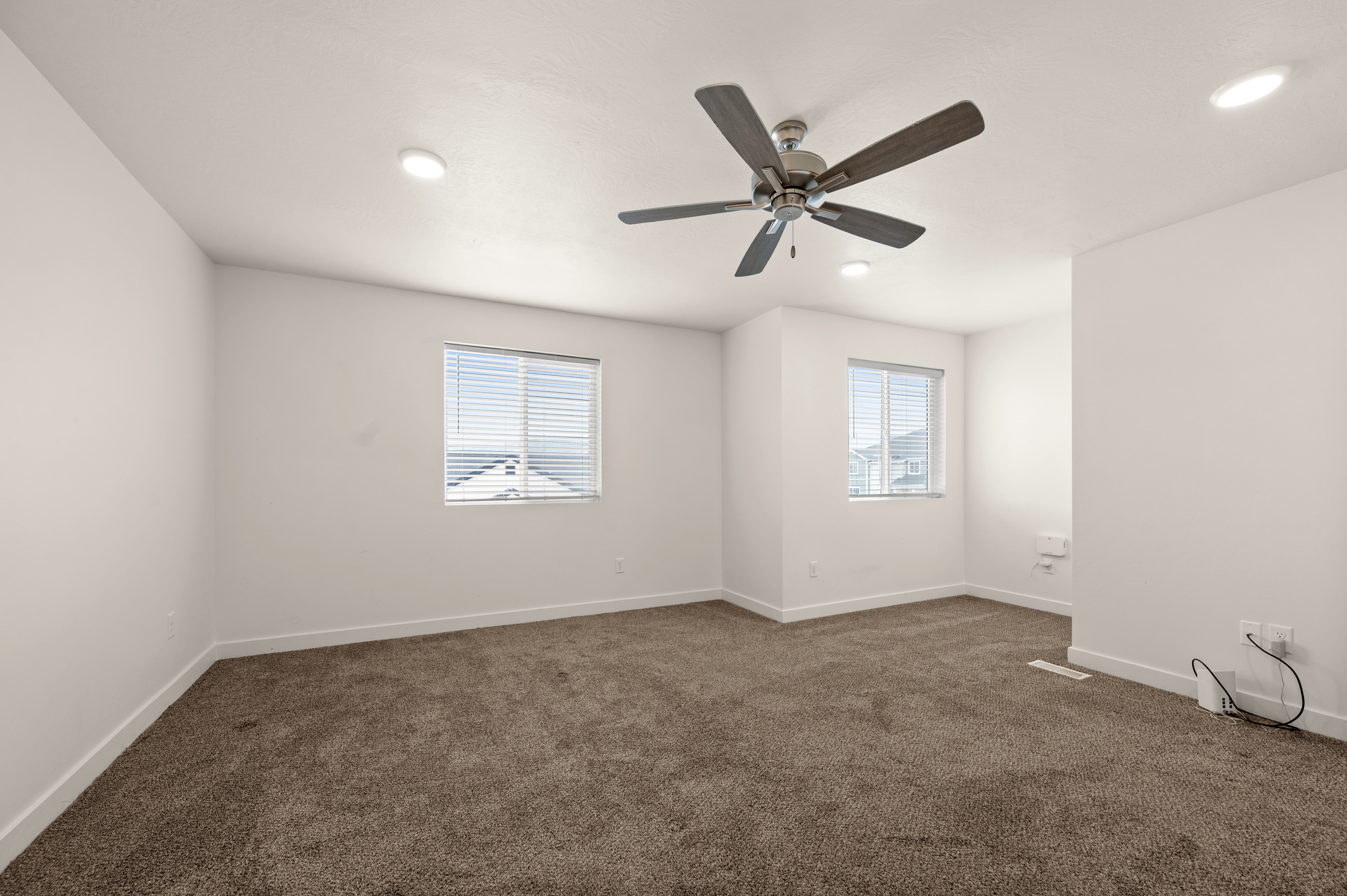 Spacious interior room featuring plush brown carpeting, crisp white walls, and a contemporary ceiling fan with integrated lighting
