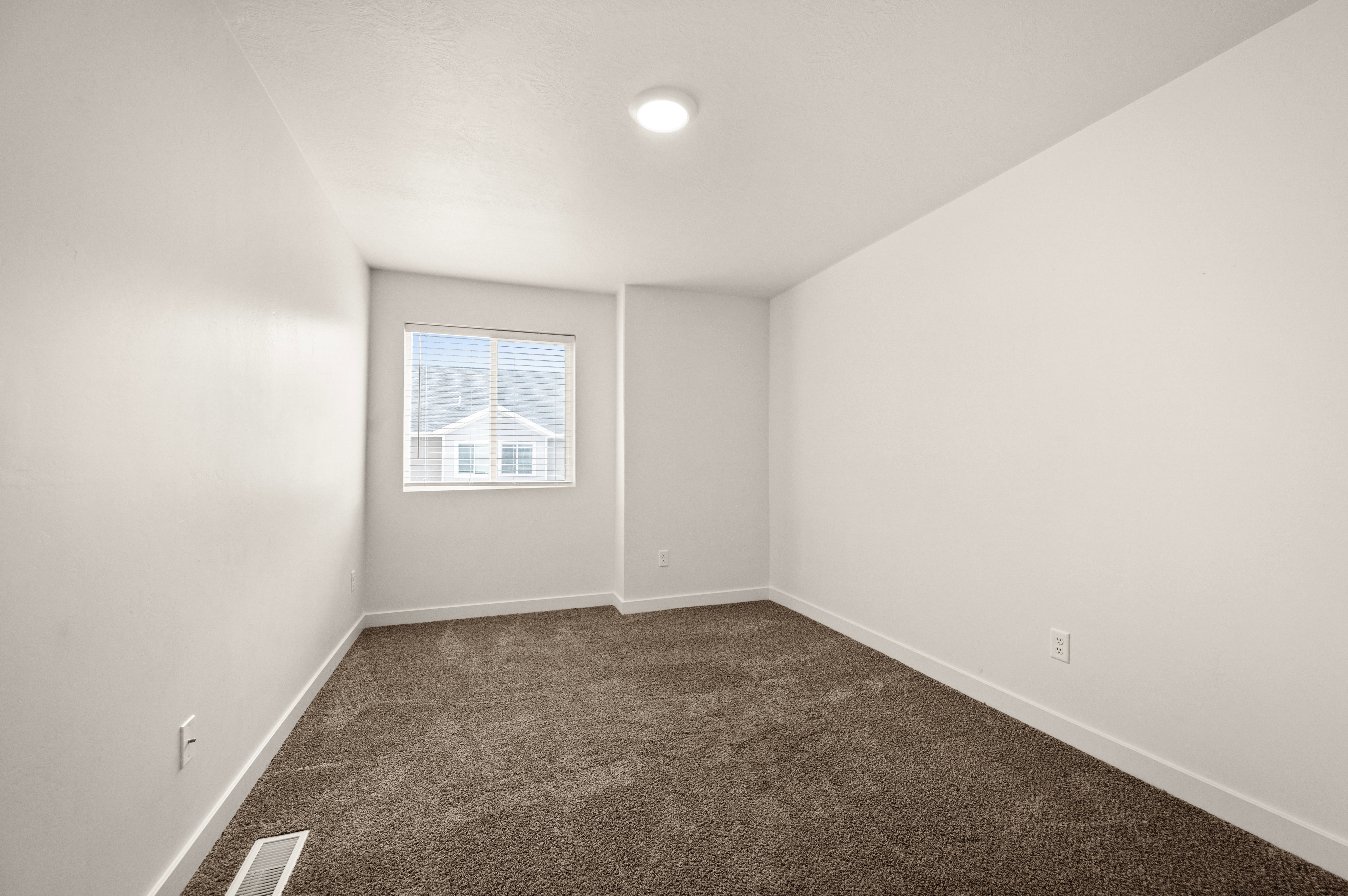 Interior room featuring neutral wall paint, a single window with blinds, brown carpet flooring, and a flush-mount ceiling light