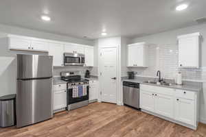 Kitchen with stainless steel appliances, white cabinets, dark wood finished floors, tasteful backsplash, and light stone countertops