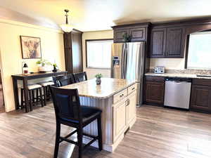 Kitchen featuring a breakfast bar, two tone cabinets, stainless steel appliances, light stone counters, and a center island