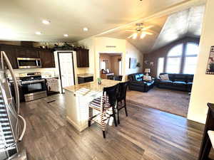 Dual tone kitchen with stainless steel appliances, two tone color scheme, light stone counters, a breakfast bar, and a ceiling fan
