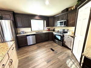 Kitchen with dark wood finish cabinetry, stainless steel appliances, light stone countertops, and dark wood finished floors