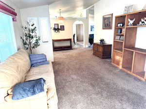 Living room with arched walkways, carpet, and lofted ceiling