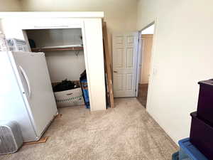 Bedroom with freestanding refrigerator, light colored carpet, and a closet
