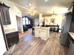 Kitchen featuring open floor plan, light stone counters, stainless steel appliances, arched walkways, and lofted ceiling