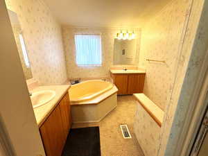 Bathroom with two vanities, a garden tub, wallpapered walls, and crown molding
