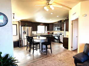 Kitchen with dark wood finish cabinetry, stainless steel appliances, a breakfast bar area, a textured wall, and ceiling fan