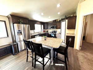 Kitchen with dark wood finish cabinets, stainless steel appliances, a breakfast bar area, a kitchen island, and lofted ceiling