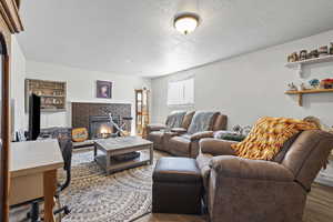 Living room with wood finished floors, a textured ceiling, and a brick fireplace
