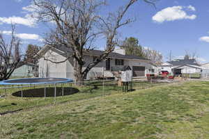Rear view of property with an attached garage, brick siding, a trampoline, a chimney, and a patio area