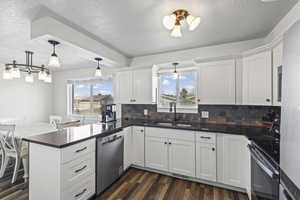 Kitchen featuring a peninsula, stainless steel appliances, white cabinetry, dark wood finished floors, and hanging light fixtures