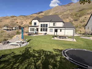 Back of house featuring a patio, an outdoor fire pit, a shingled roof, and a mountain view