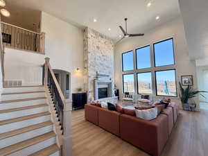 Living room with a high ceiling, a stone fireplace, light wood-style floors, ceiling fan, and recessed lighting