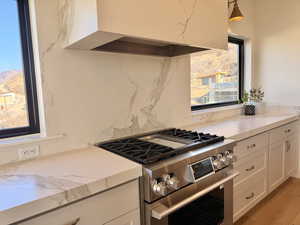 Kitchen featuring extractor fan, high end stove, white cabinetry, decorative backsplash, and light stone countertops